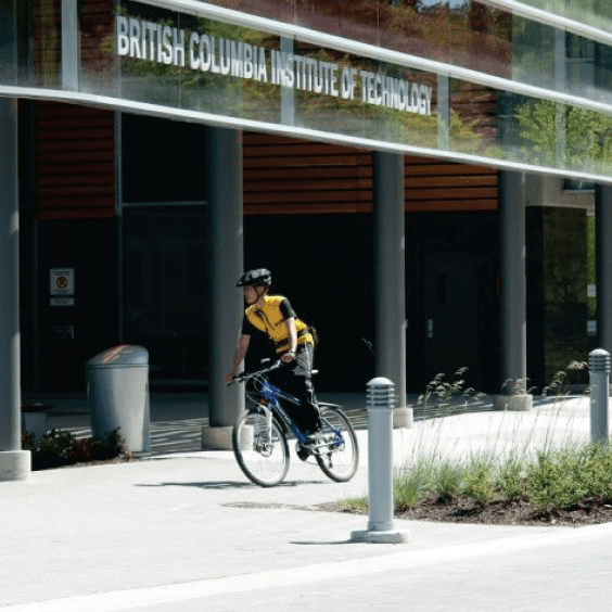 man on a bike riding past the exterior of British Columbia Institute of Technology